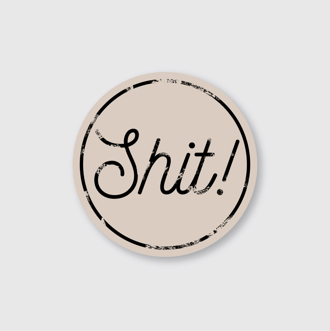 This beige, round, die-cut vinyl sticker features the word "Shit!" in black cursive with a distressed style. Designed by artists, it includes a thin black border on a weather-resistant light gray background.