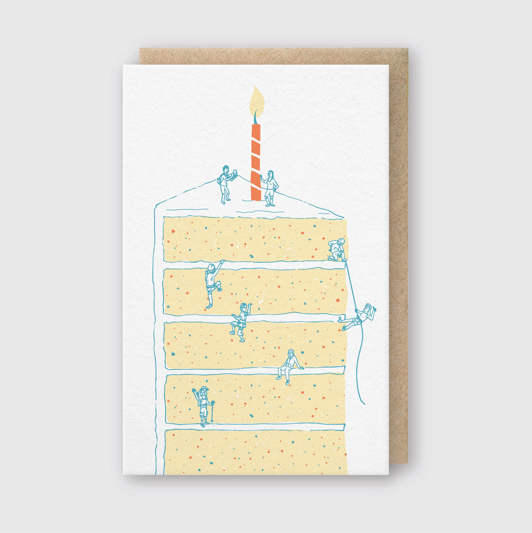 The Cake Climbers Greeting Card features a playful illustration of a slice of cake with a single candle. Tiny figures dubbed "Cake Climbers" are shown scaling the cake using ropes and ladders, turning it into an imaginative mountain climbing adventure. This charming card is crafted with FSC Certified Paper and utilizes letterpress printing techniques for a high-quality finish.