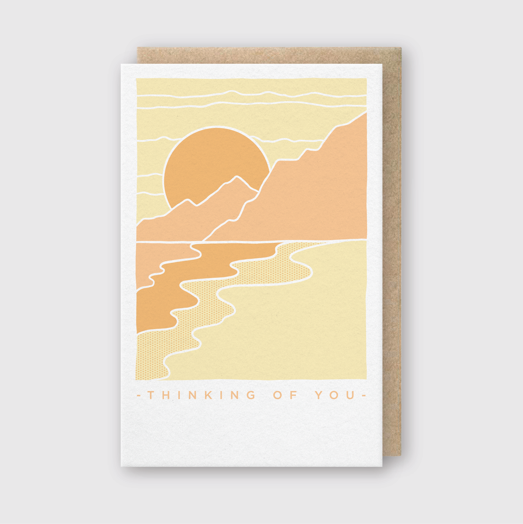 The Thinking of You Scenery Greeting Card features a minimalist design with an abstract landscape showing a sun setting behind mountains and a river. The warm shades of orange and yellow enhance its charm, with "Thinking of You" elegantly inscribed below. Handcrafted in Seattle, it's perfect for sending thoughtful wishes.