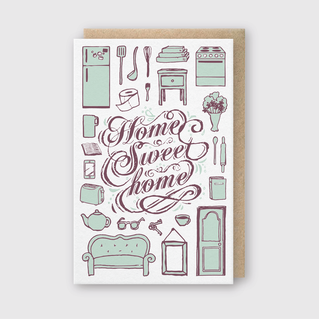Introducing the **Home Sweet Home Greeting Card**, an illustrated card featuring the phrase "Home Sweet Home" surrounded by delightful drawings of household items like a refrigerator, stove, and couch. This charming letterpress creation uses green and purple hues on a white background to beautifully capture the cozy essence of home life.