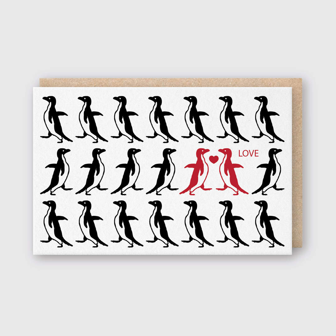 The Love Penguins Card features black penguin silhouettes encircling two red penguins gazing at each other with a heart in between and the word "LOVE." Handcrafted in Seattle, this card comes with a brown envelope, making it an ideal choice for animal enthusiasts.