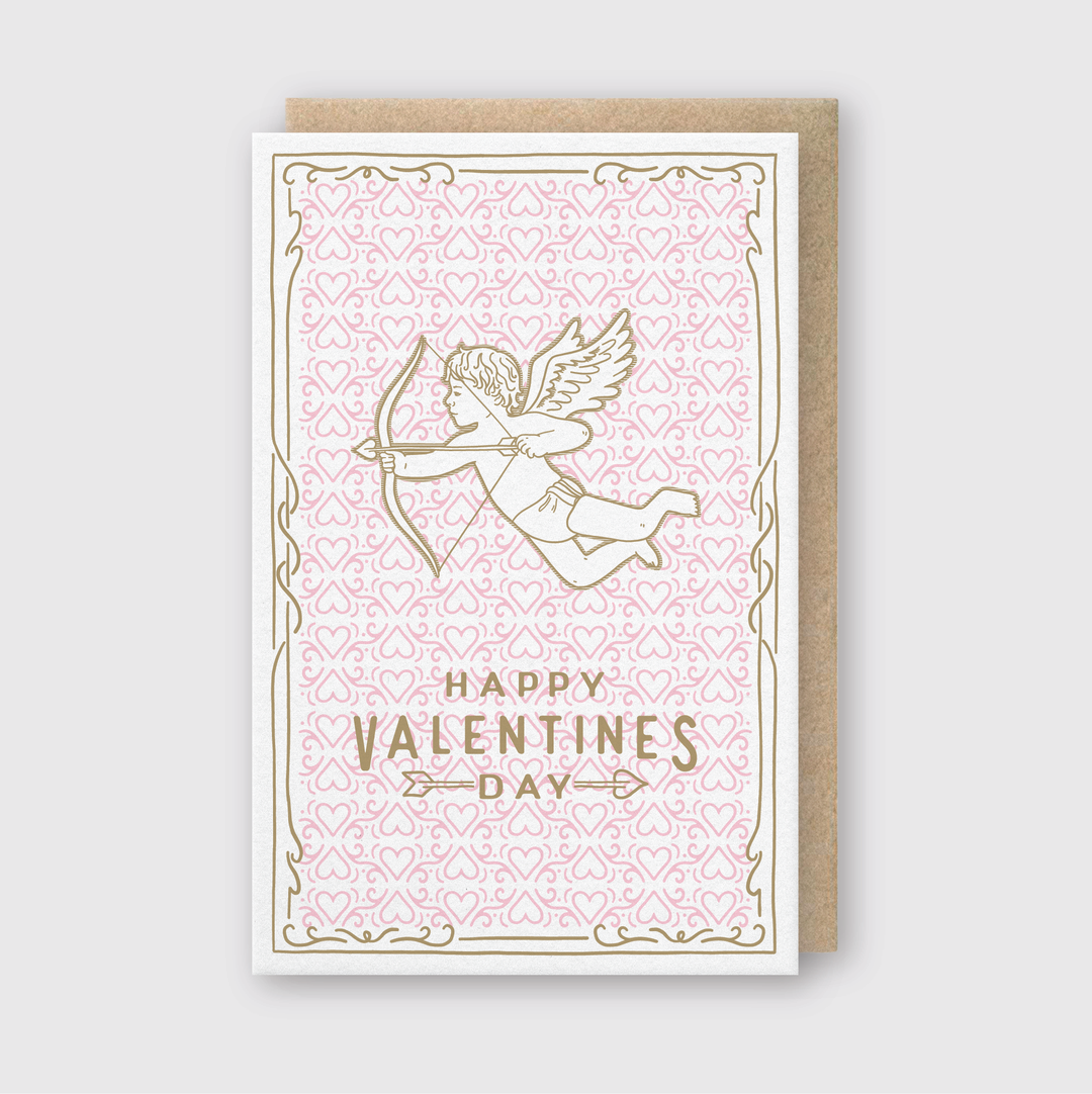 Discover the Valentine's Day Cupid Greeting Card, a beautifully handcrafted piece from Seattle. This card highlights a gold cupid with a bow and arrow against a pink patterned backdrop. The elegant "Happy Valentine's Day" message is written in gold letters and surrounded by a decorative border. It comes with an eco-friendly recycled Kraft envelope.