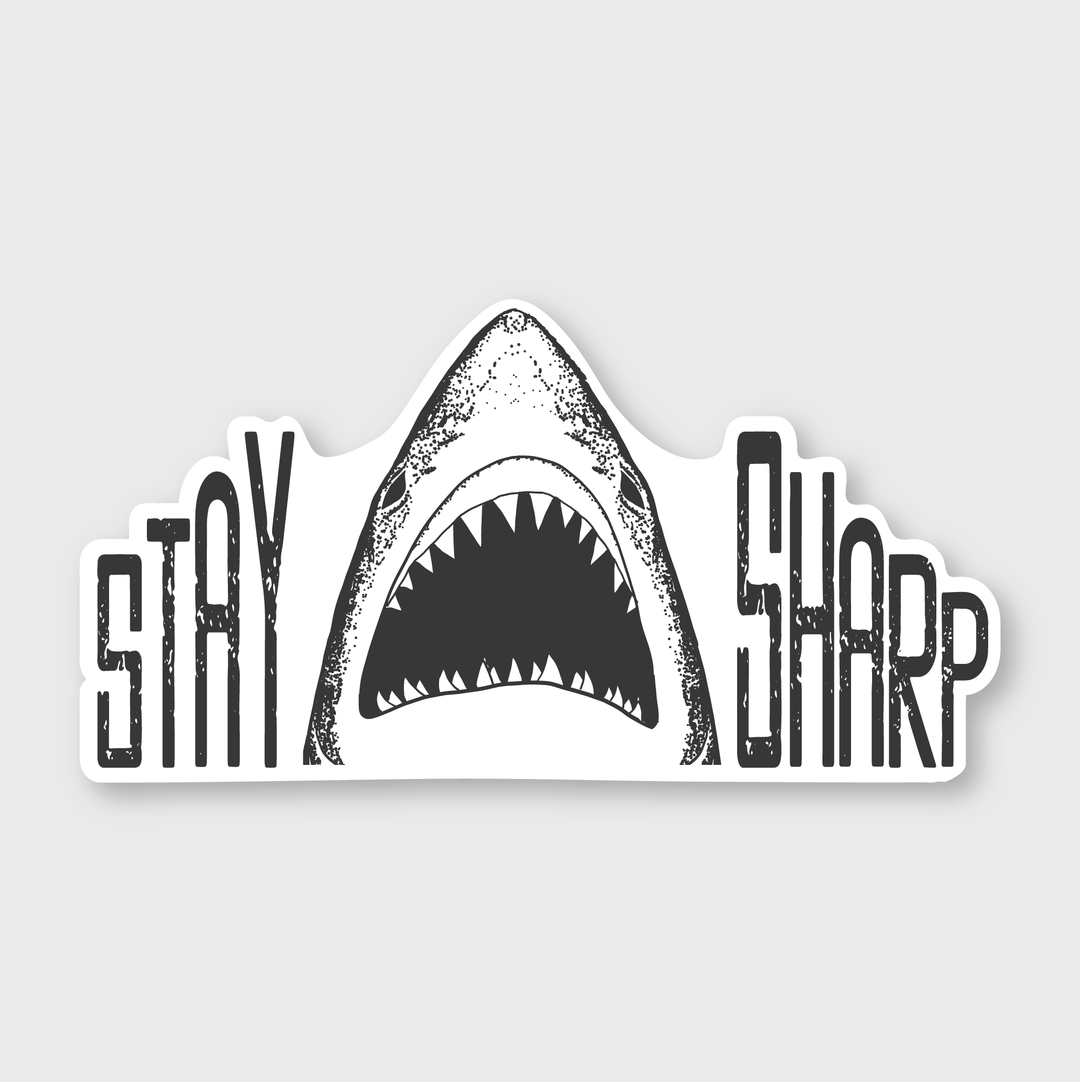 Introducing the "Stay Sharp Shark Sticker," featuring a bold black and white design with a shark's mouth open between the words "Stay" and "Sharp" in striking, stylized font. This sticker showcases a jagged outline to complement the shark's teeth, ensuring outdoor-rated durability.