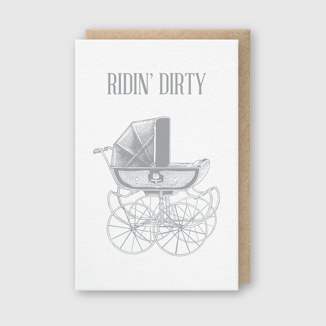 Introducing the Ridin' Dirty Greeting Card: This handcrafted card showcases a vintage baby stroller with large wheels and playful "RIDIN' DIRTY" text at the top, making it a perfect choice for humorously celebrating new parenthood.