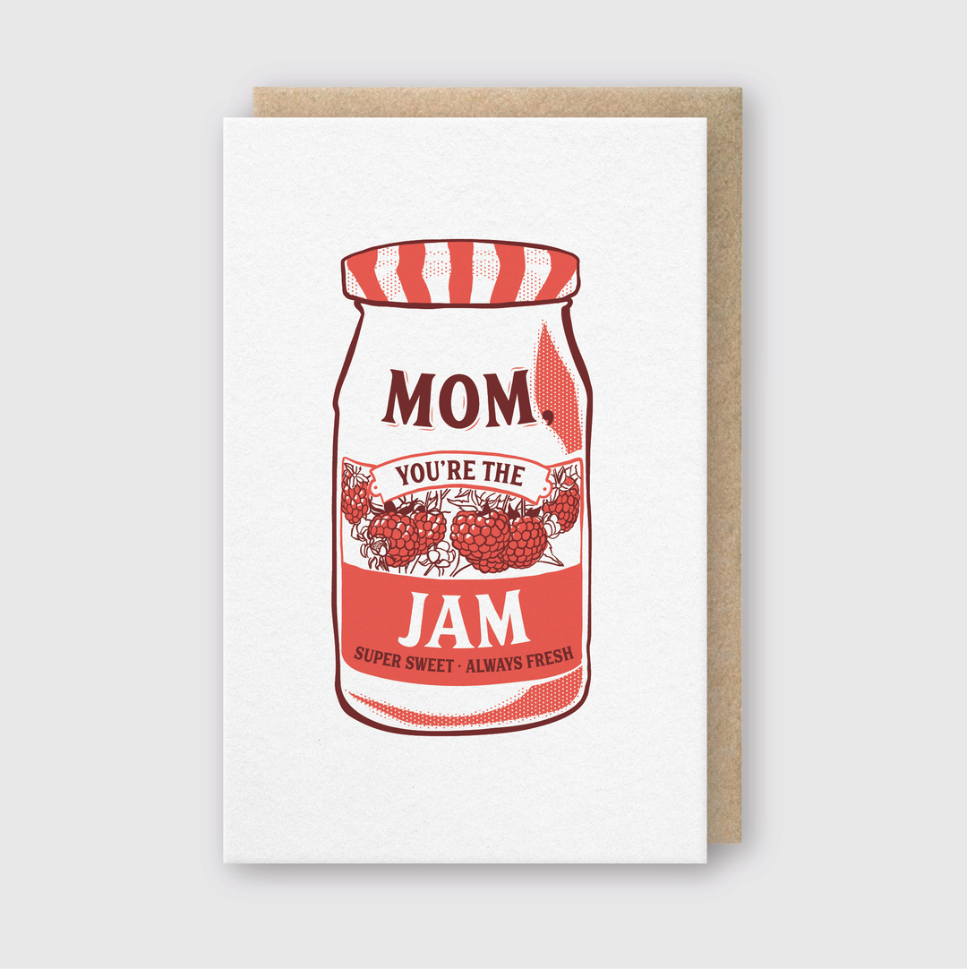 The "Mom You're The Jam Letterpress Card" from Pike Street Press features a charming illustration of a jam jar labeled "Mom, You're the Jam." The design is accented with raspberries and includes the phrase "Super Sweet - Always Fresh" on a plain white background. Ideal for music-loving moms, this handcrafted card comes from Seattle and is coupled with a brown envelope.