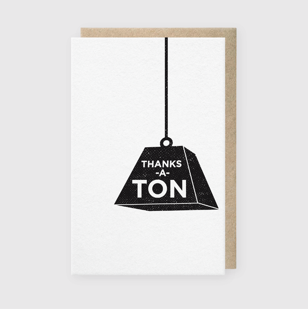 The "Thanks a Ton Weight Greeting Card" features premium letterpress craftsmanship with an eye-catching design of a large black weight hanging from a string. The card prominently displays the words "THANKS A TON" on a simple gray background, highlighting the artisanal quality often associated with Seattle.