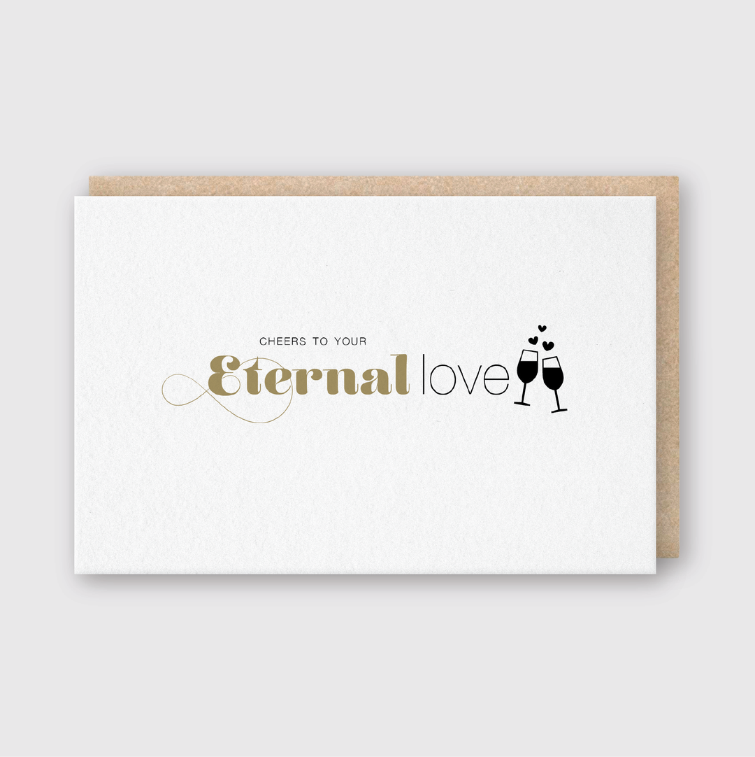 This greeting card features a charming illustration of two champagne glasses clinking, adorned with hearts above. It includes the elegant message "Cheers to your Eternal love" in graceful fonts. This handcrafted card is made with soy-based inks and comes with a brown envelope, set against a light gray background.