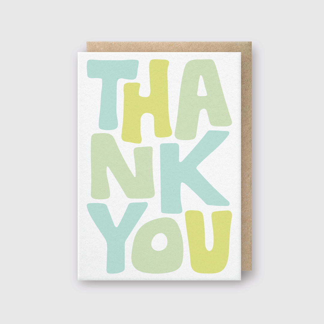 The Thank You Abstract Letters Greeting Card features a hand-printed design with "THANK YOU" in large, bold letters in pastel shades of green, blue, and yellow. This vibrant design contrasts with a simple gray background and comes with a partially visible brown envelope.