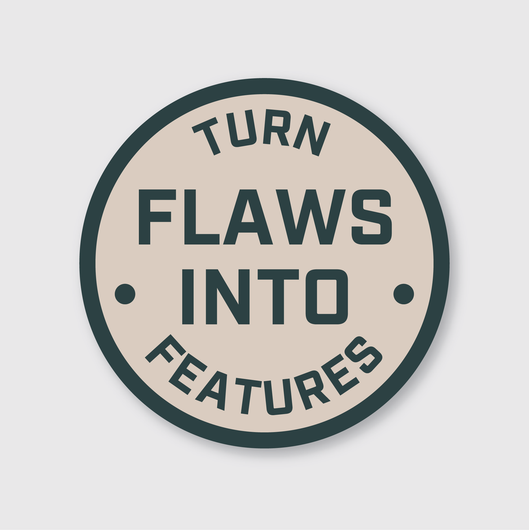 The "Flaws Into Features Sticker" is a circular die-cut vinyl sticker with a beige background and a dark green border. It features the bold, capitalized message "TURN FLAWS INTO FEATURES," offering a simple yet motivational touch. Made from high-quality vinyl, this sticker is designed to be weather-resistant.