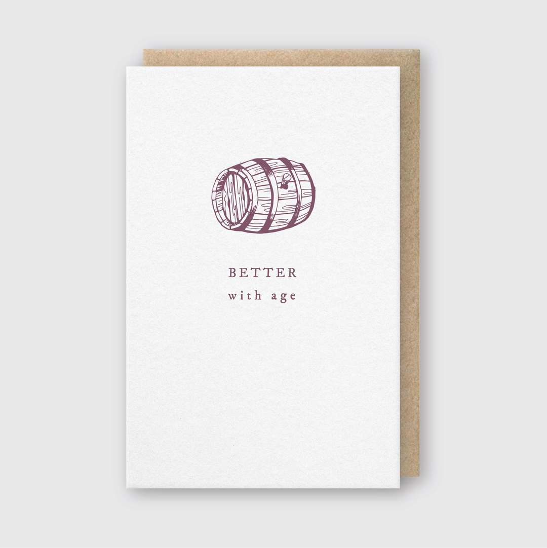 The Better With Age Greeting Card showcases a letterpress-embossed illustration of a wooden barrel. Below the image, the phrase "BETTER with age" is elegantly printed. The card comes with a recycled kraft envelope that complements its light gray background beautifully.