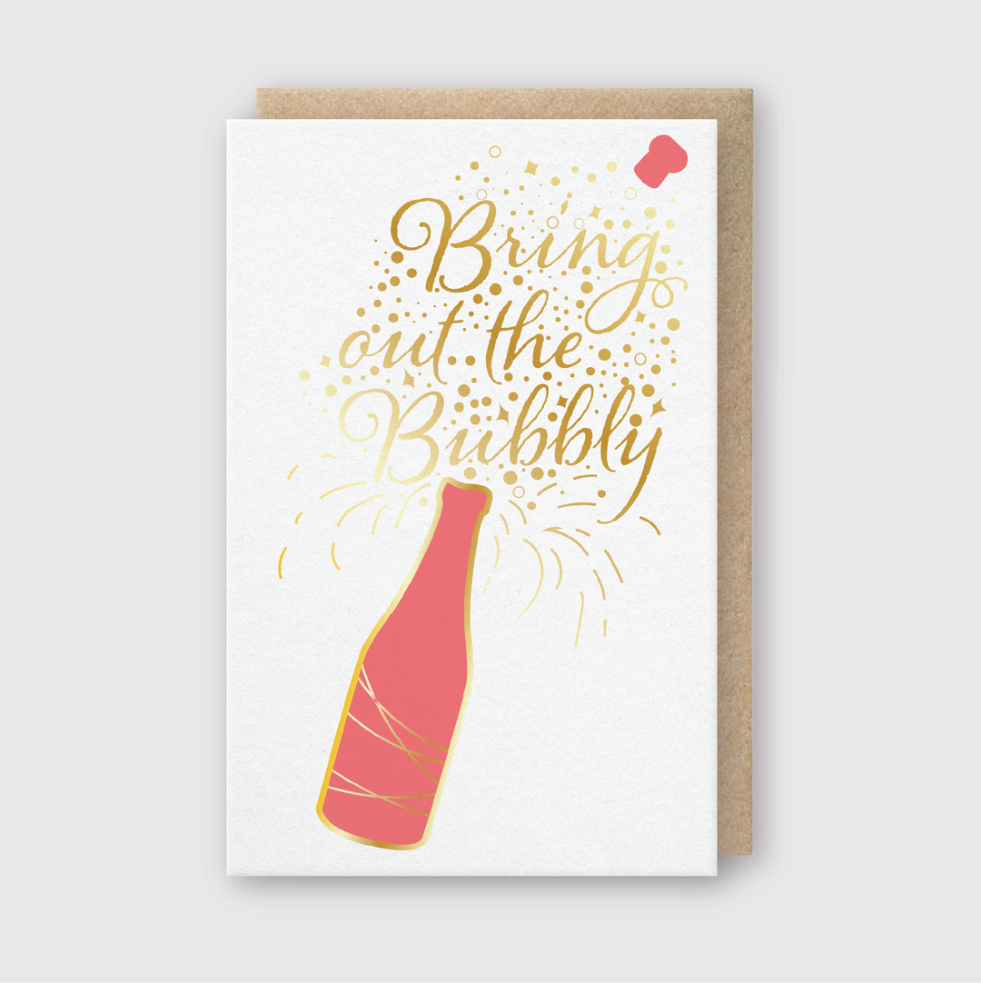 The Bring Out the Bubbly Foil Greeting Card features a lively design with a champagne bottle popping, accented by bright pink and gold colors. It is beautifully adorned with shimmering gold sparkles and includes the cheerful cursive message "Bring out the Bubbly.