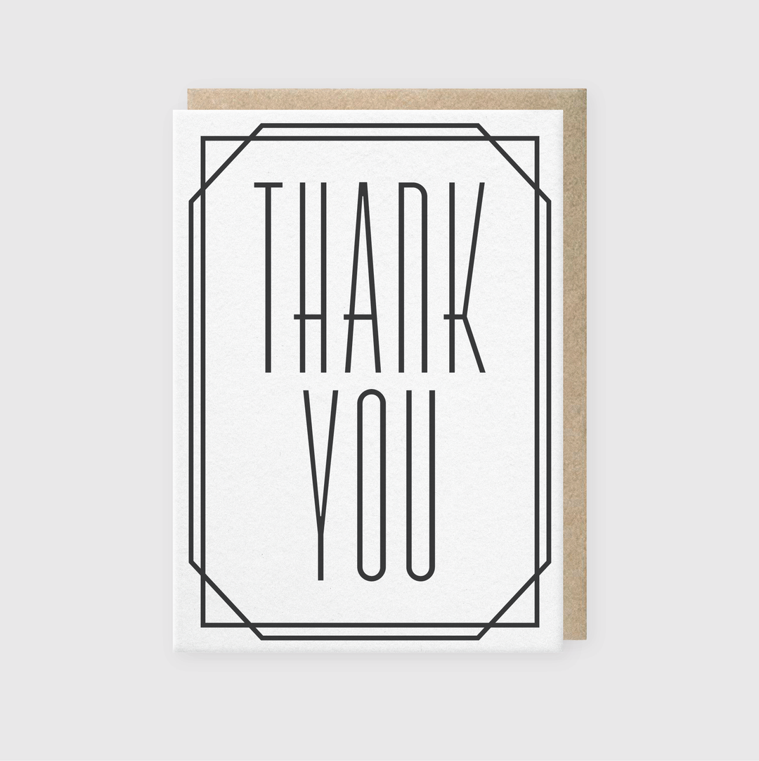 Introducing the Pike Street Press "Thank You Deco Greeting Card": a premium card with a minimalist white front and bold black lettering that reads “THANK YOU” within a geometric border. Handcrafted in Seattle, it comes with a brown envelope, partially visible behind it.