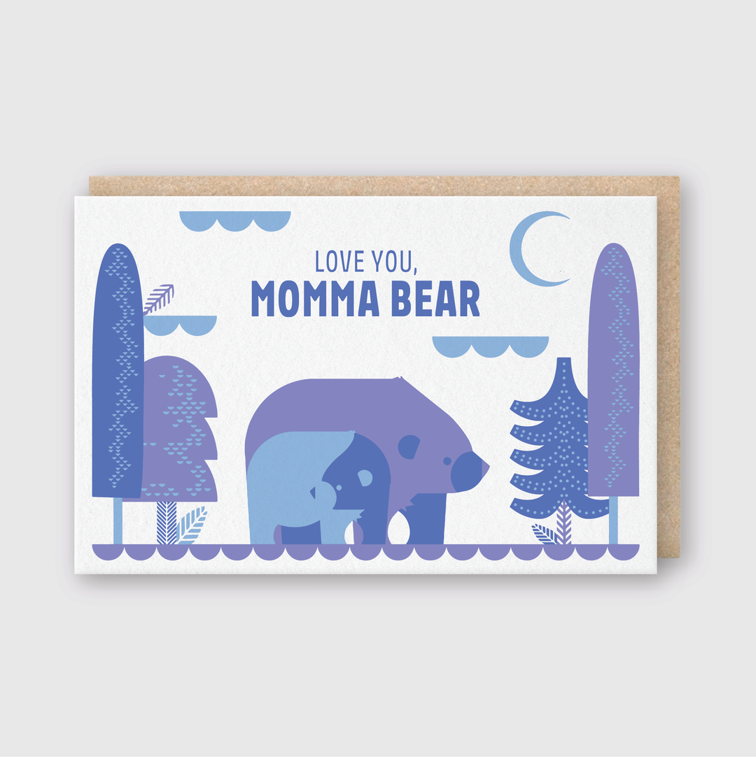 The "Love You, Momma Bear Greeting Card" features an illustration of a mother bear and cub in shades of blue and purple, walking among stylized trees. The card includes the phrase "Love you, Momma Bear." Crafted using premium letterpress techniques in Seattle, it presents a minimalistic and playful design with elements like a crescent moon and clouds.