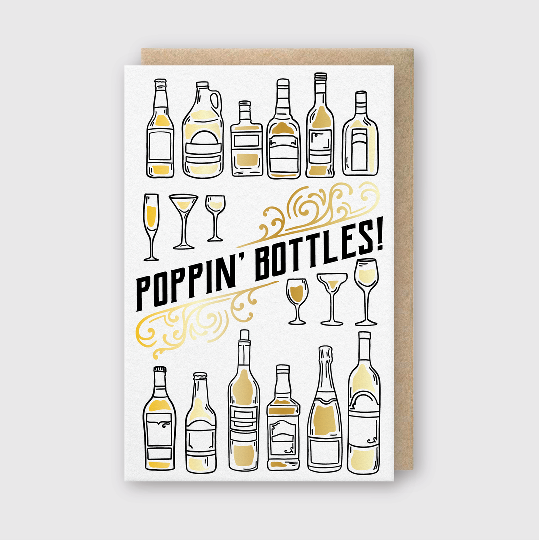 The Poppin' Bottles Foil Greeting Card showcases a beautiful letterpress design with champagne bottles and glasses highlighted in gold. The phrase "Poppin' Bottles!" is prominently featured at the center, complemented by an ornamental flourish underneath.