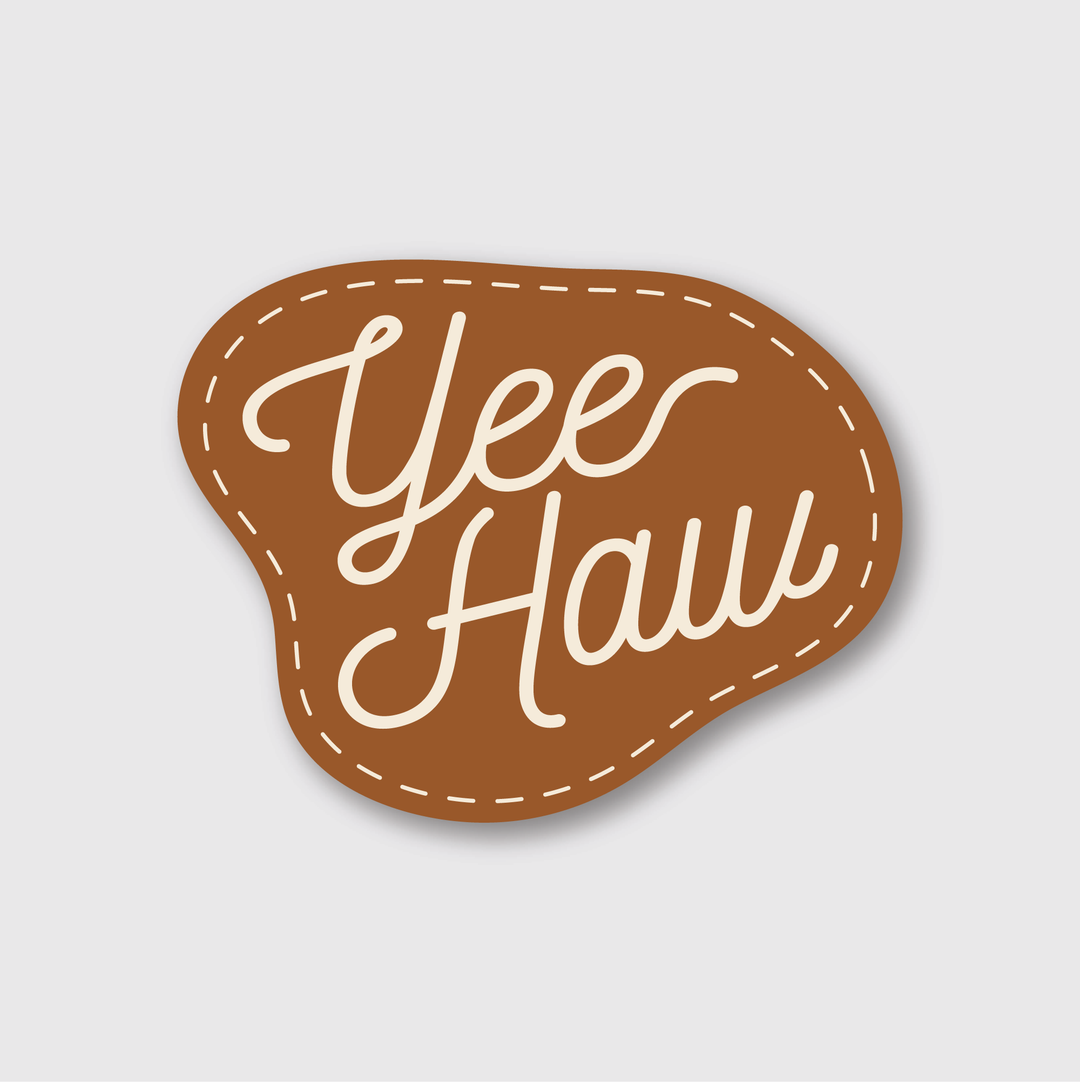 This high-quality die-cut vinyl sticker features a brown, irregular shape with "Yee Haw" elegantly scripted in white cursive, accentuated by a dashed white outline. The design rests against a plain light gray background and is enhanced by a laminated matte finish for superior durability and style.