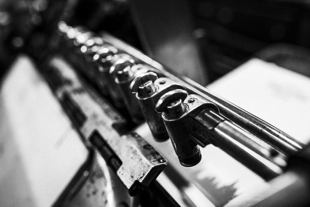 In the close-up black and white image, the vintage typewriter's metal typebars and intricate mechanisms are prominently displayed. The focus on the levers and type slugs highlights their mechanical elegance, showcasing the detailed craftsmanship of the device. The monochromatic tone enhances the timeless appeal and historical significance of this classic piece of technology.