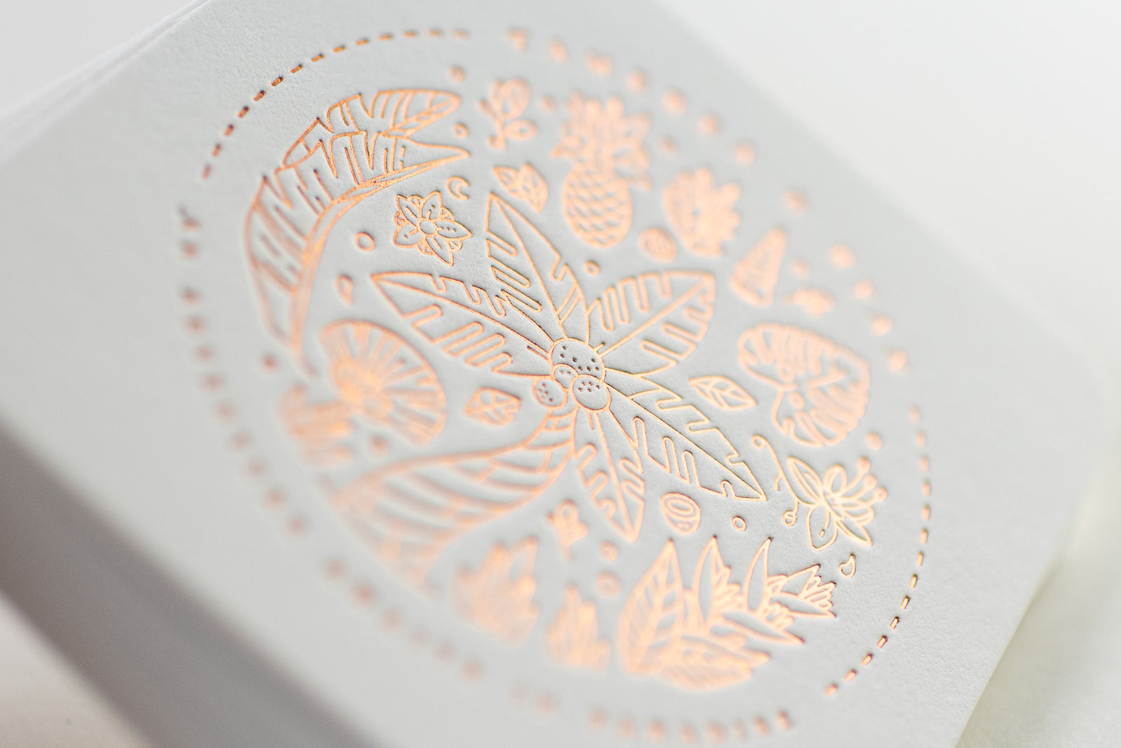 This description is of an embossed card featuring detailed botanical designs, including leaves, flowers, and fruits arranged in a circular pattern. The design is accentuated with a soft coppery sheen that highlights the intricate details of the embossing process.