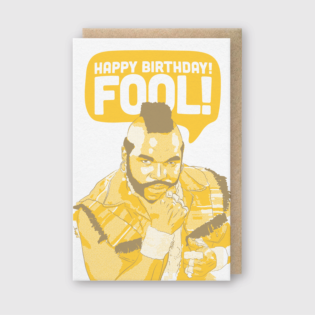 The "Happy Birthday Fool Greeting Card" features a muscular man with a mohawk and beard in a sleeveless jacket, his fist near his chin. A speech bubble above him presents the bold yellow message: "Happy Birthday Fool!" using letterpress techniques.