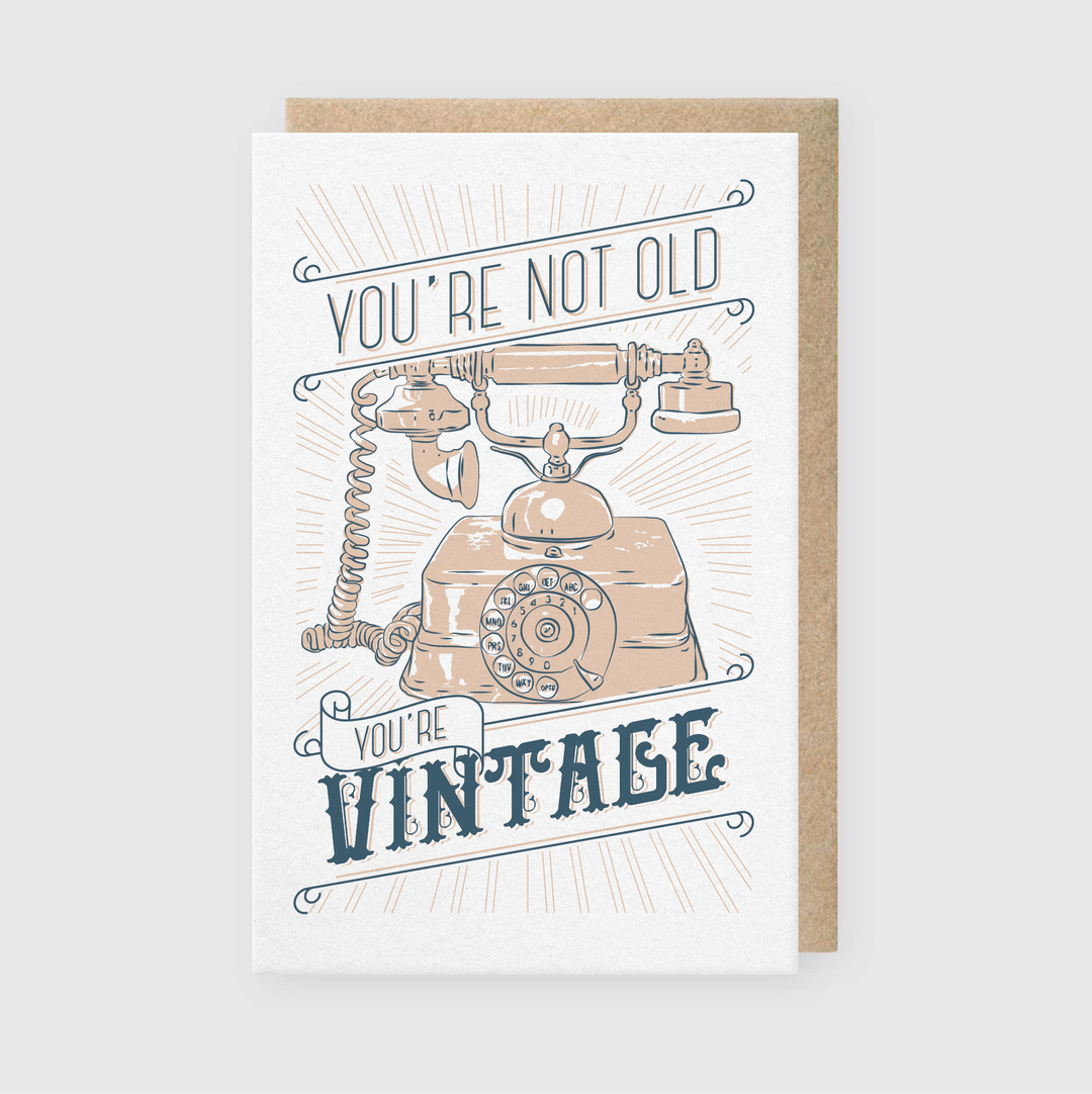 The "Not Old, Vintage" illustrated card features a vintage rotary phone and the message "You're Not Old, You're Vintage." Perfect for birthday greetings, it utilizes a retro color scheme of blue and beige inspired by classic letterpress printing on a simple background.