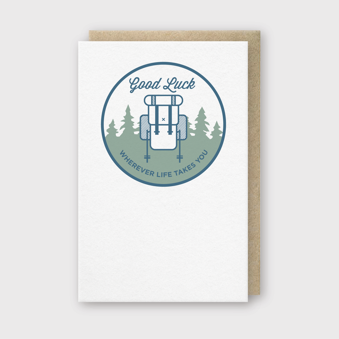 The "Good Luck Backpack Greeting Card" by Pike Street Press features a charming circular design with a backpack and trees, along with the message "Good Luck Wherever Life Takes You." Accompanied by a brown envelope, it beautifully captures the spirit of adventure and well wishes.
