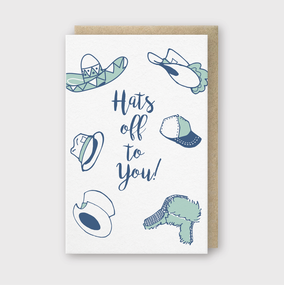 The "Hats Off to You Greeting Card" features the phrase "Hats off to you!" surrounded by illustrations of various hats, including a sombrero, baseball cap, and top hat in blue and green shades. Set against a light background with a brown border, this card is perfect for celebrating with style.