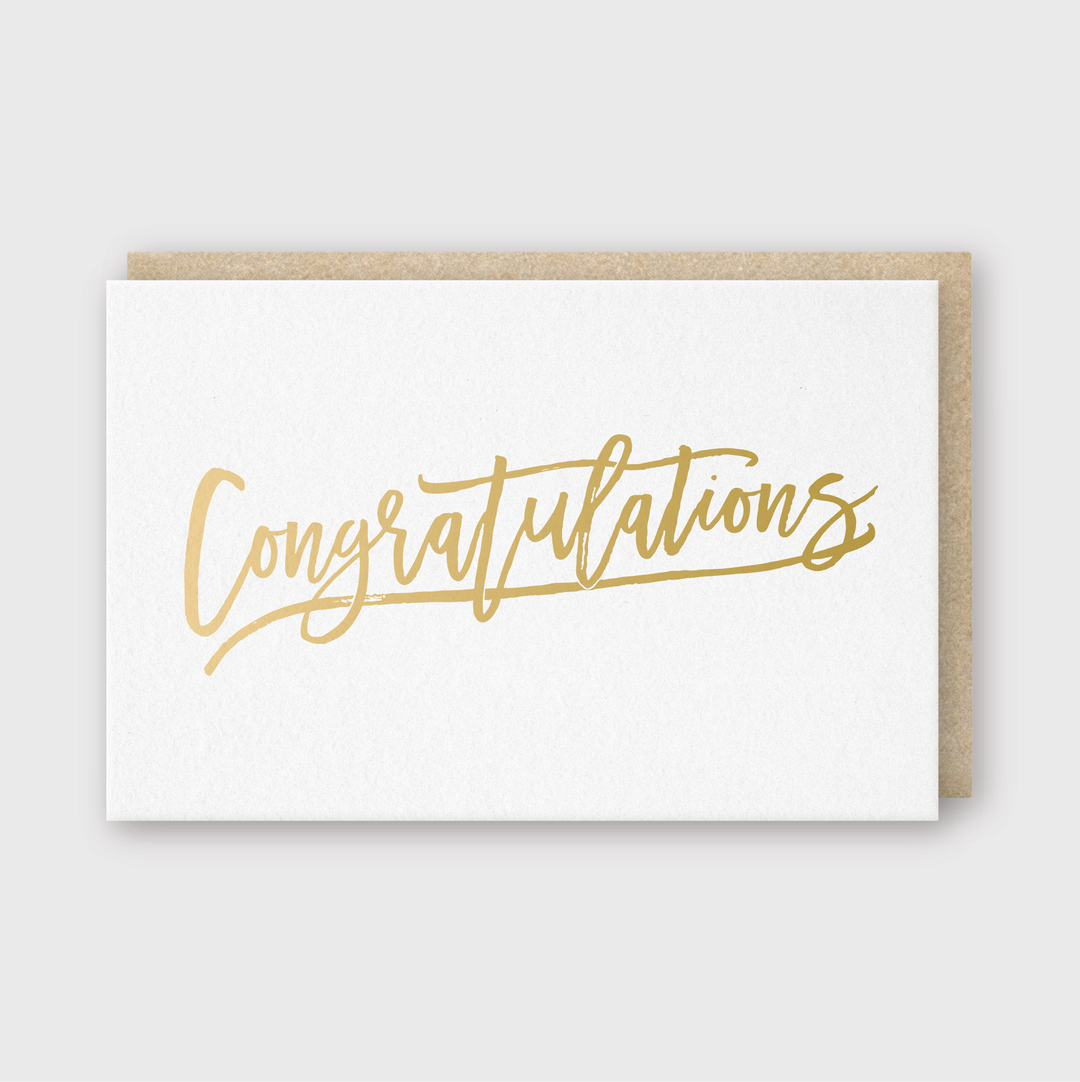 The "Congrats Gold Foil Greeting Card" is adorned with a stylish gold script that says "Congratulations," offering a touch of elegance. It comes with a brown envelope, all set against a light gray backdrop.