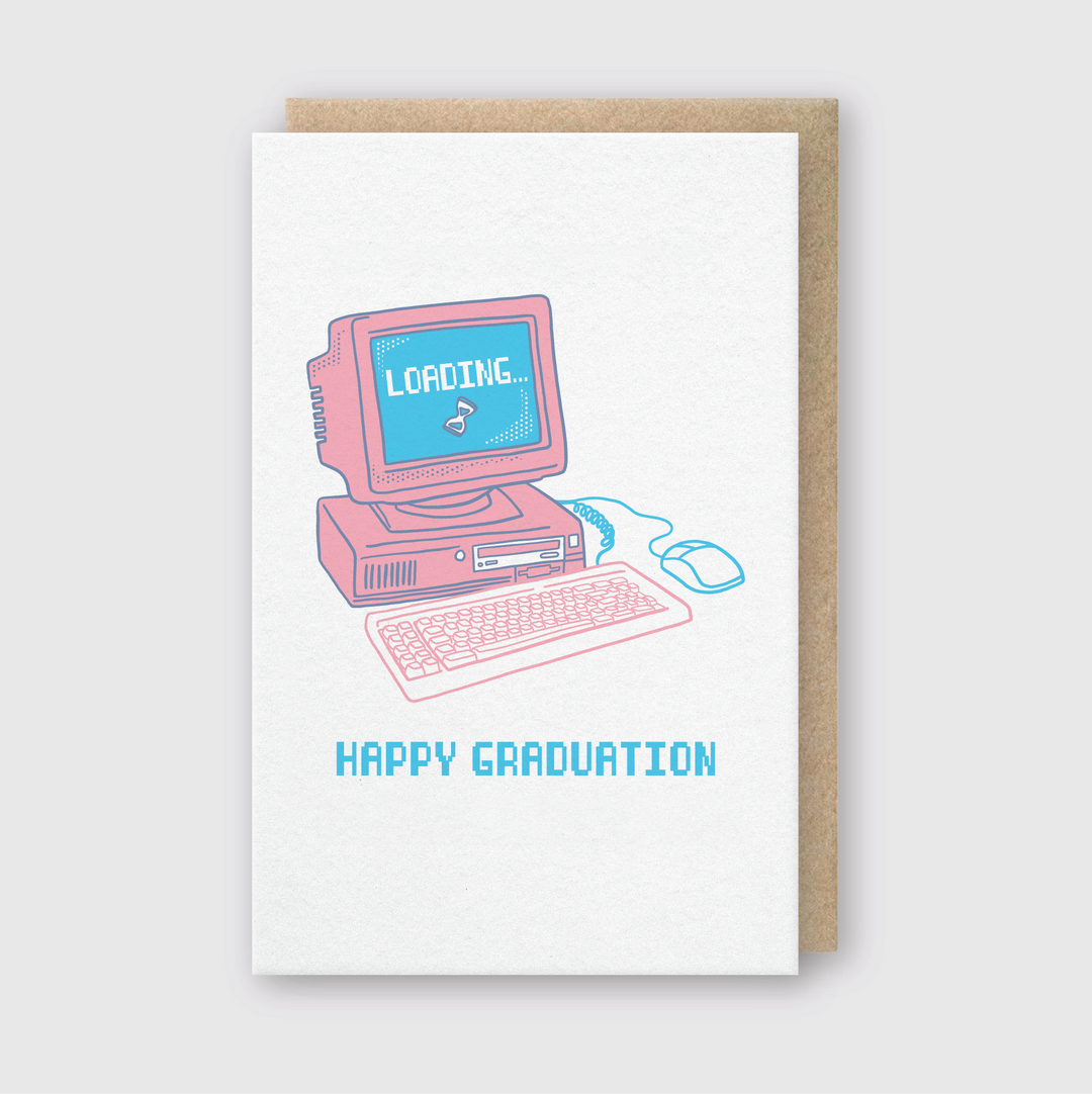 The Retro Computer Grad Greeting Card features a vintage computer illustration with "Loading..." on the screen and "HAPPY GRADUATION" written beneath in blue. The design includes a pink keyboard, mouse, and monitor. It is handcrafted in Seattle and comes with a Recycled Kraft Envelope for an eco-friendly touch.