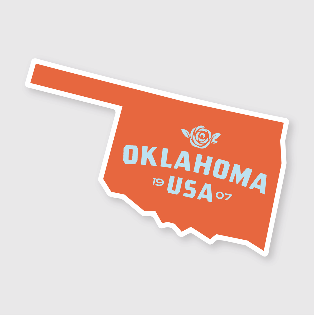 This weather-resistant orange vinyl sticker is shaped like Oklahoma and features "OKLAHOMA USA 1907" alongside a rose graphic in white text on a light gray background. It's perfect for proudly displaying your connection to Oklahoma anywhere.