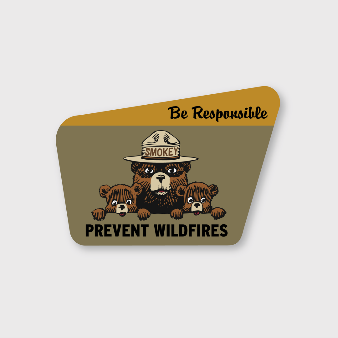 The Smokey Bear Be Responsible Sticker features an illustration of a bear in a ranger hat, accompanied by two bear cubs. The message "Be Responsible" is prominently displayed at the top, while "Prevent Wildfires" appears at the bottom. This die cut vinyl sticker is water and weather resistant and has a muted green and yellow background.