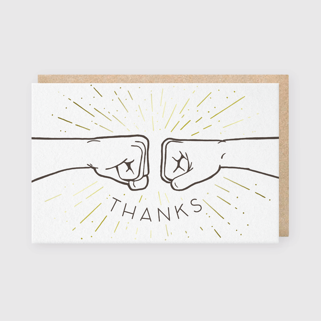 A charming illustration of two fists bumping with rays radiating outward symbolizes a warm gesture, with "THANKS" boldly displayed below. This Fist Bump Thanks Greeting Card is skillfully hand printed using letterpress techniques and comes on a white card paired with a brown envelope.