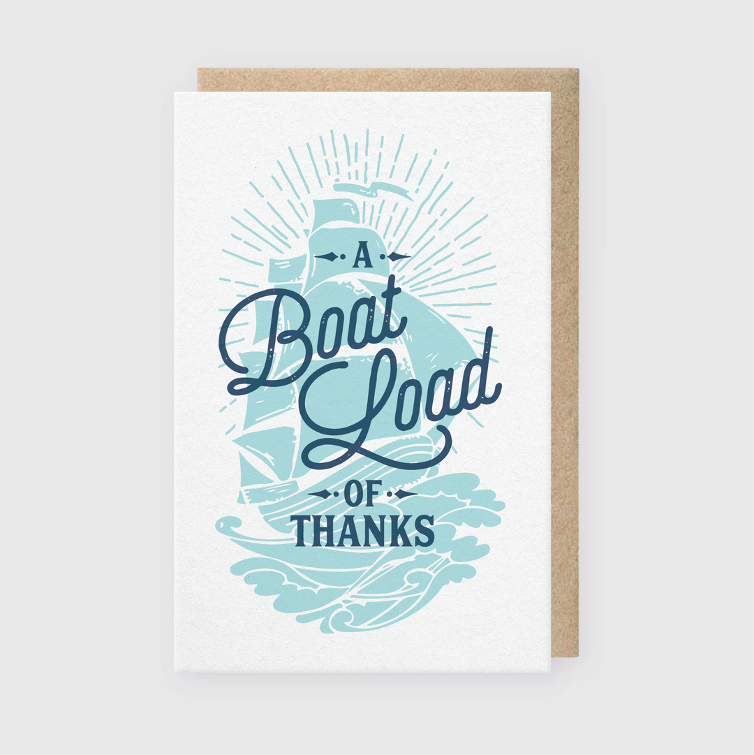 The Boatload of Thanks Greeting Card features an illustration of a sailing ship navigating vibrant waves. The card includes stylized blue text that reads "A Boatload of Thanks" set against a light grey background, capturing the essence of gratitude with a nautical theme.