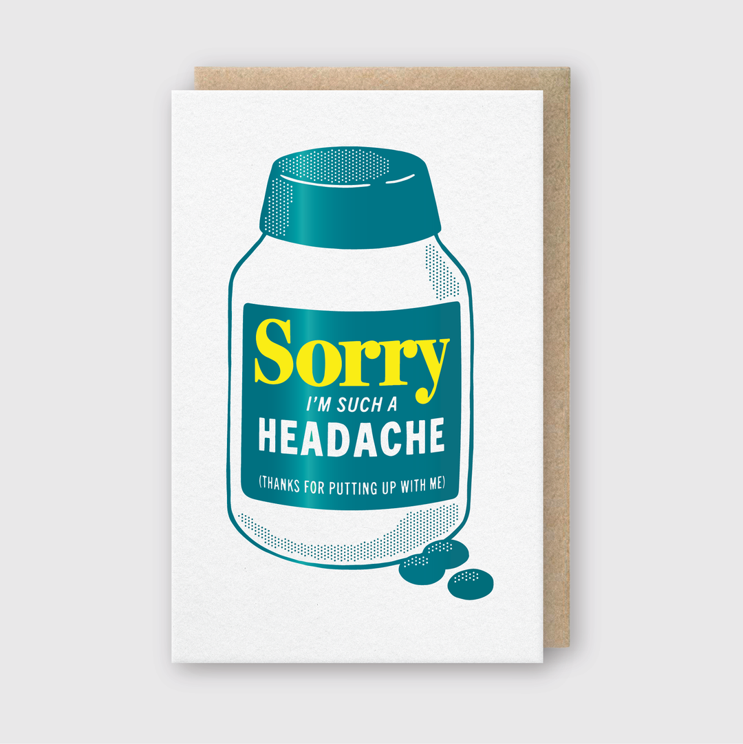 The Pike Street Press "Sorry I'm Such a Headache" greeting card is a handcrafted item that showcases an image of a medicine bottle and pills, humorously labeled with "Thanks for putting up with me." It features a gray background and comes with an eco-friendly recycled kraft envelope.