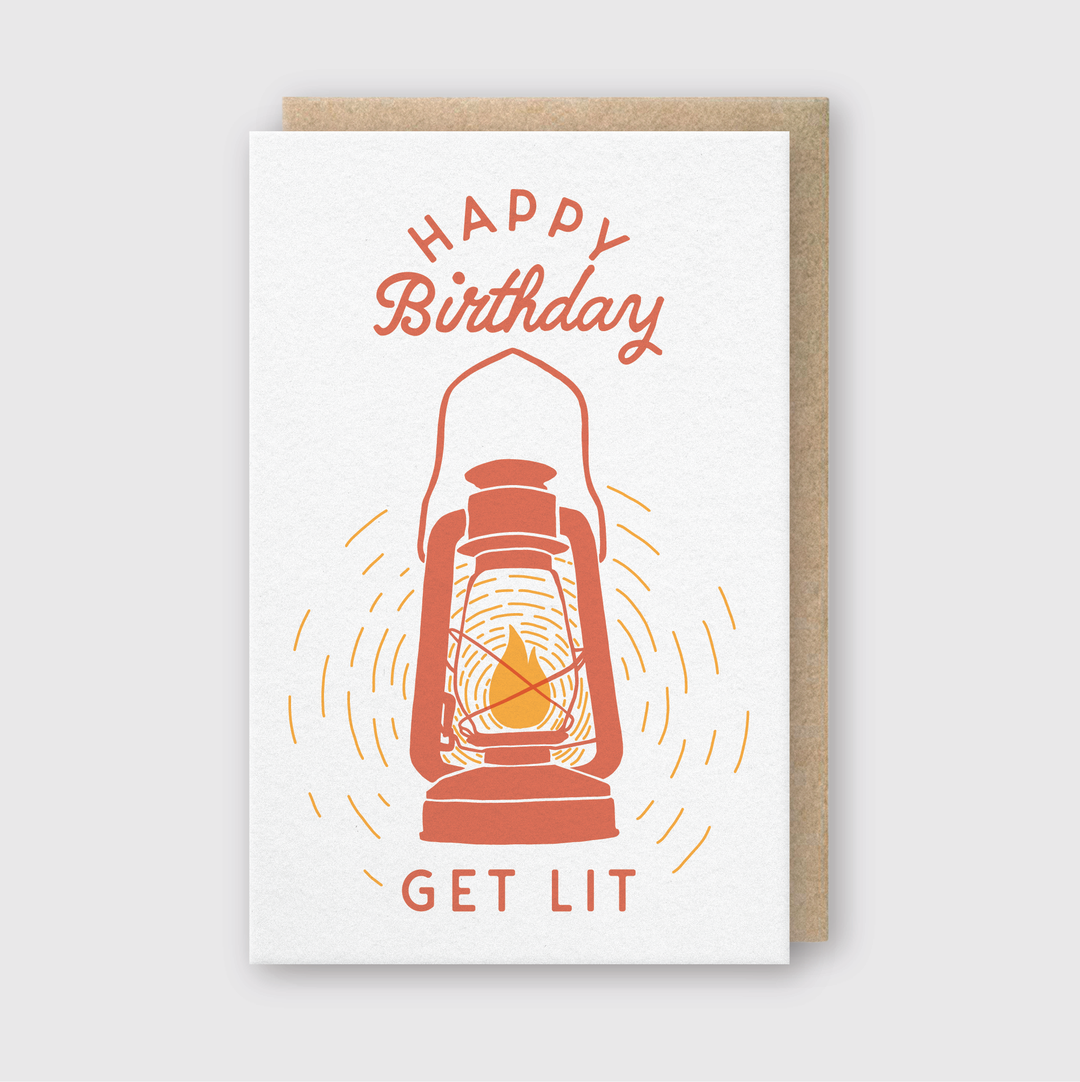 The Get Lit Lantern Greeting Card features a vintage lantern illustration in orange, created with letterpress techniques. "Happy Birthday" is prominently displayed above the lantern, while "Get Lit" is written underneath. This handcrafted Seattle card offers an elegant design set against a gray background.