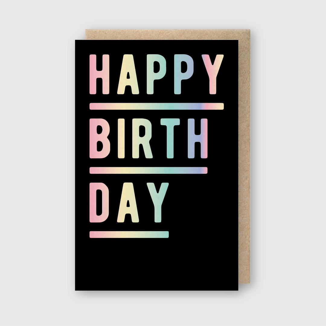 A Holographic Foil Birthday Greeting Card showcases the words "HAPPY BIRTH DAY" in large, bold, multicolored gradient letters against a sleek black background. The card is slightly open, revealing a Recycled Kraft Envelope positioned behind it.