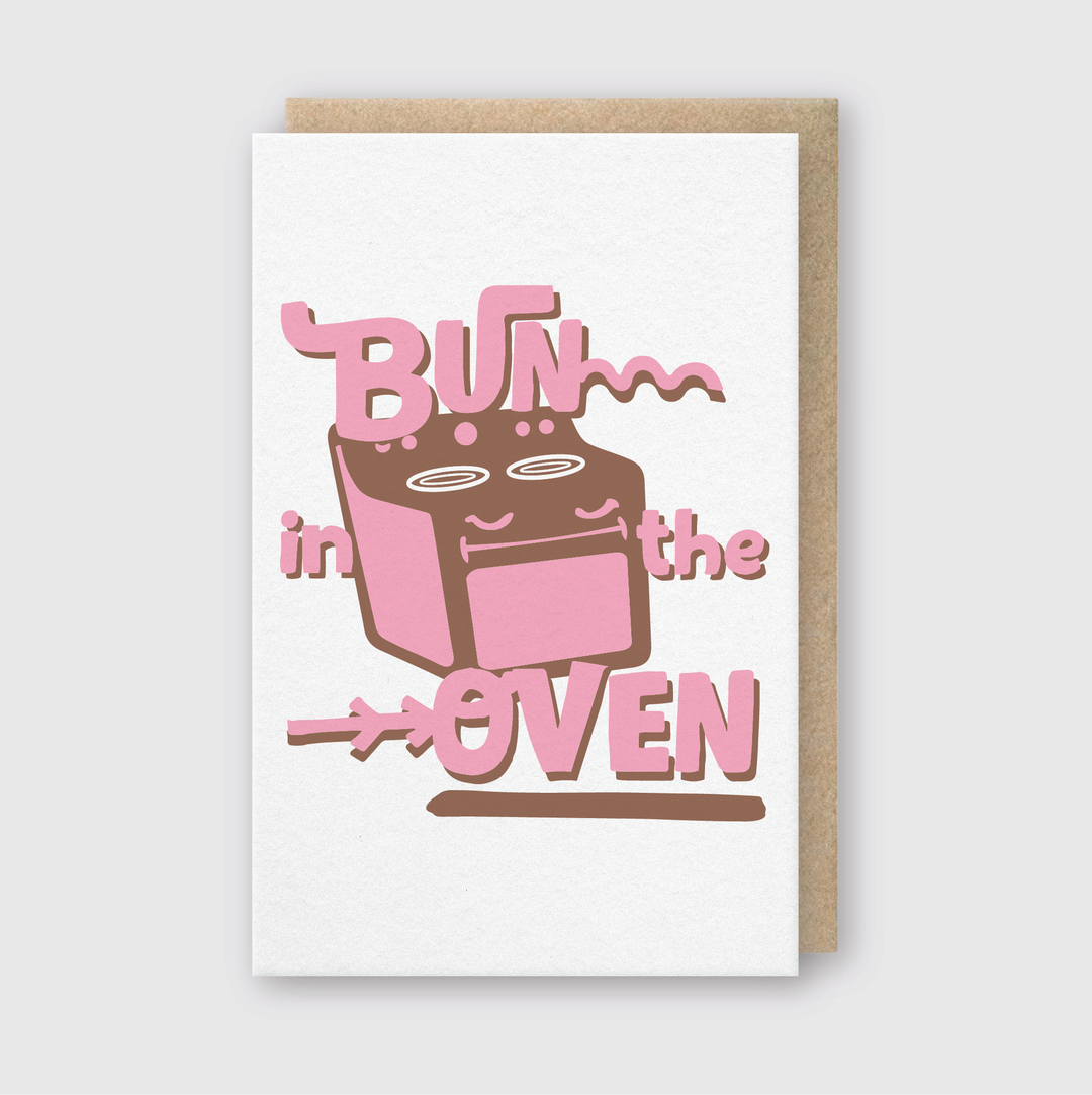 The "Bun In the Oven Greeting Card" showcases a charming pink oven illustration with the phrase "Bun in the Oven" in bold pink lettering on a light gray background.