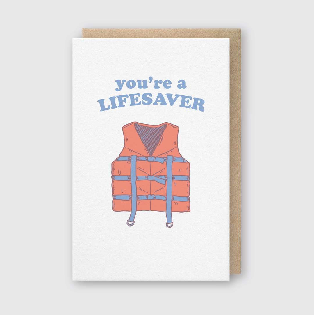 The "You are a Lifesaver" Greeting Card features an illustration of an orange life jacket in the center. Above it, the phrase "You're a Lifesaver" is written in blue text. This card is made with high-quality letterpress techniques and includes a brown envelope, all set against a plain background.