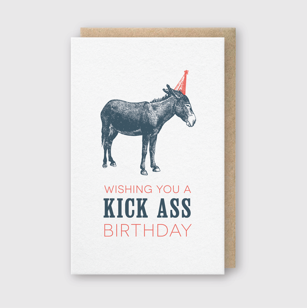 The Kick Ass Birthday Card showcases a whimsical donkey in a party hat, created with letterpress techniques on FSC Certified Paper. It features bold and playful text that says, "Wishing you a kick ass birthday!