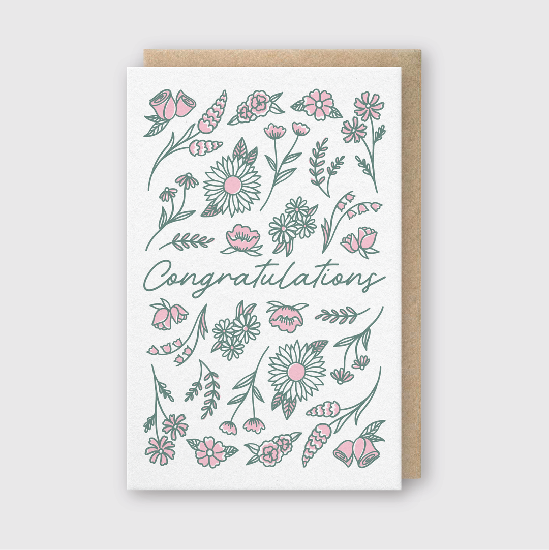Here is the product description for the Pike Street Press "Congratulations Flowers Greeting Card":
The card features elegant script surrounded by charming illustrations of green and pink flowers and leaves, creating a delightful visual appeal. It comes paired with a complementary brown envelope, all set against a light gray background for an understated yet sophisticated presentation.