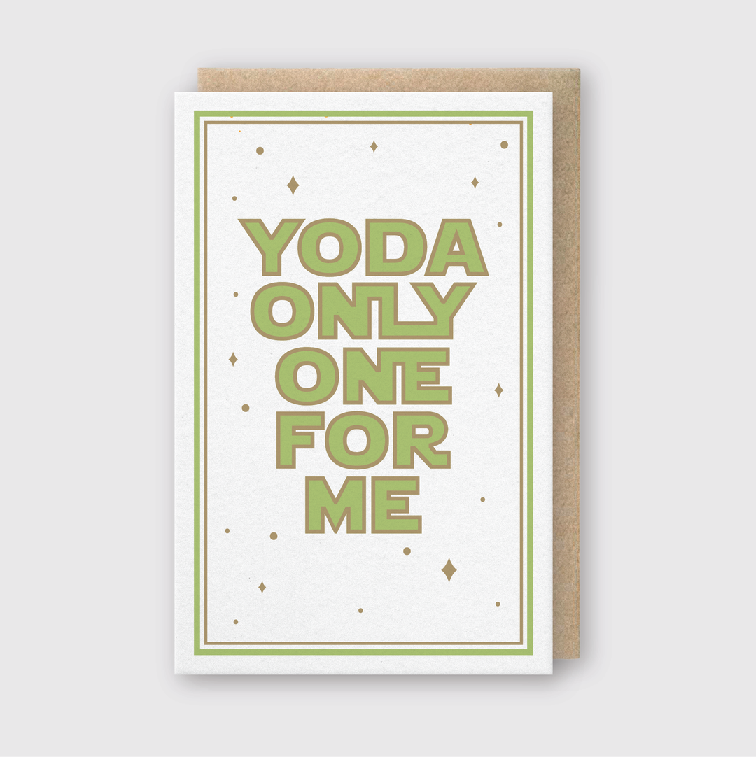 Introducing the "Yo-da Only One For Me Greeting Card," featuring bold green letters on a white backdrop adorned with delicate gold stars and encircled by a lustrous gold border. It is paired beautifully with a recycled Kraft envelope, all presented against a light gray background.