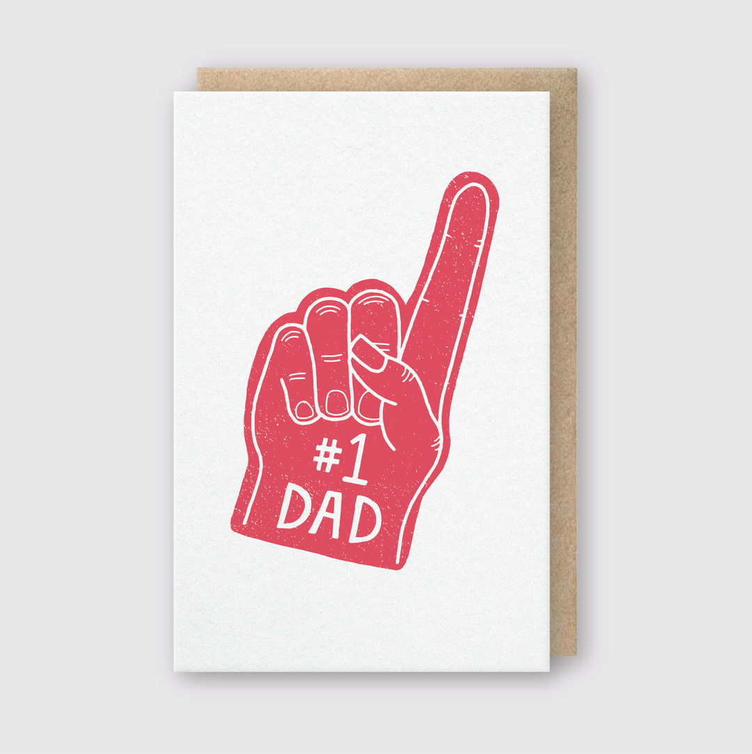 Introducing the #1 Dad Foam Finger Greeting Card: a delightful Father's Day tribute featuring an illustration of a red foam finger proudly displaying #1 with "DAD" on the palm. Handcrafted in Seattle, this card is set against a light gray background, making it the perfect gesture for your number one dad.