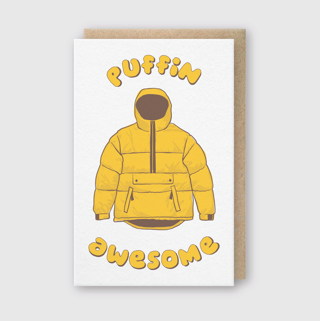The Puffin Awesome Greeting Card features a charming illustration of a yellow puffer jacket. "PUFFIN" is cheerfully displayed above the jacket, while "awesome" playfully dances below, all on a plain background. This card is perfect for those who appreciate unique and lively designs.