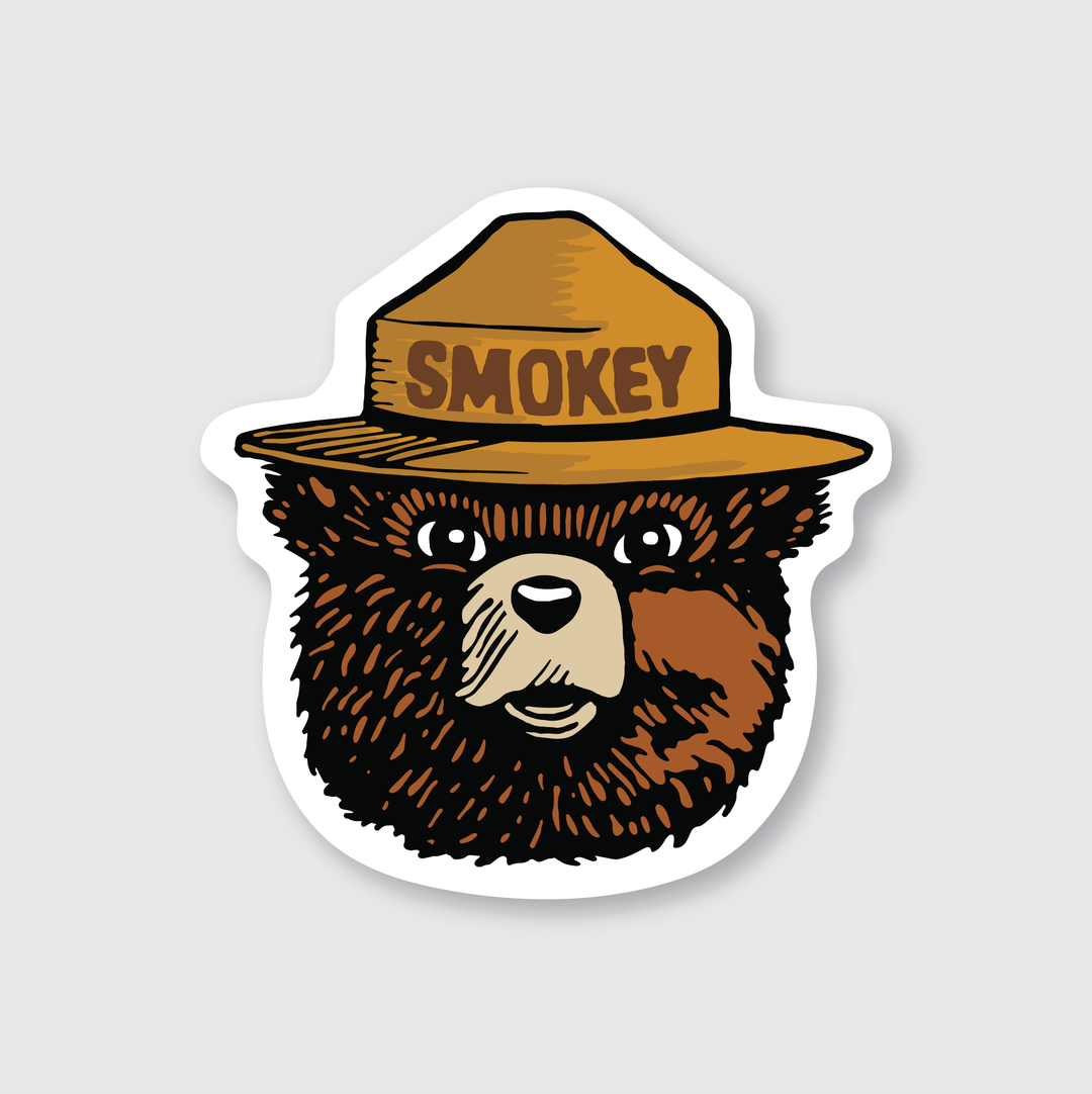 This description features a cartoon bear wearing a brown ranger hat with "SMOKEY" written on it. Set against a light gray background, the bear has a friendly expression, making it an excellent Smokey Bear sticker. Made from die-cut vinyl, this weather-resistant sticker is ideal for outdoor enthusiasts.