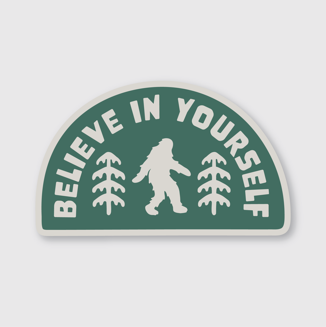 The Believe in Yourself Sticker by Pike Street Press features a die-cut vinyl design with a green background, highlighting a silhouette of Bigfoot surrounded by pine trees. The phrase "Believe in Yourself" elegantly arches above the figure. Created by talented artists, this weather-resistant sticker inspires adventure and resilience.