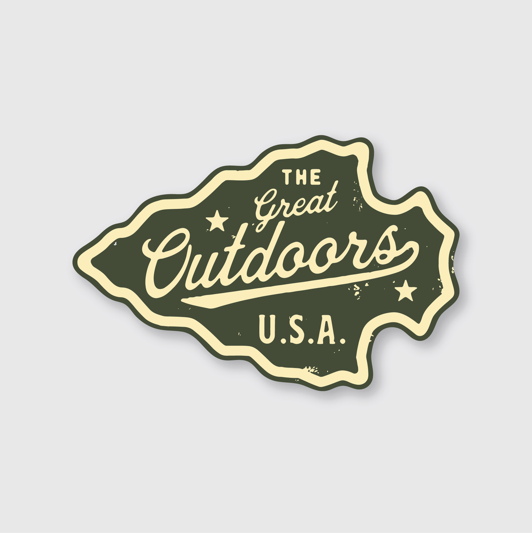 Introducing the "Great Outdoors Arrowhead Sticker"—this vintage-style adventure sticker, shaped like rugged terrain, showcases "The Great Outdoors U.S.A." in bold letters. Its dark green background, cream-colored text, and decorative stars embody the spirit of exploration. Ideal for those in search of an outdoor vinyl sticker with timeless charm.