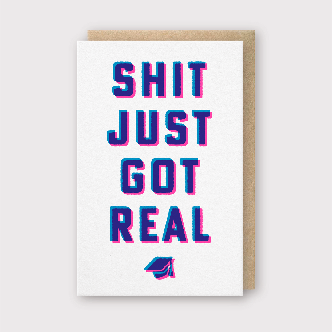 The "Shit Just Got Real" Greeting Card showcases vibrant blue and pink text on a pristine white background, with an endearing illustration of a graduation cap for added charm. Expertly handcrafted in Seattle using FSC Certified Paper, it features a delicate light gray backdrop for an elegant finish.