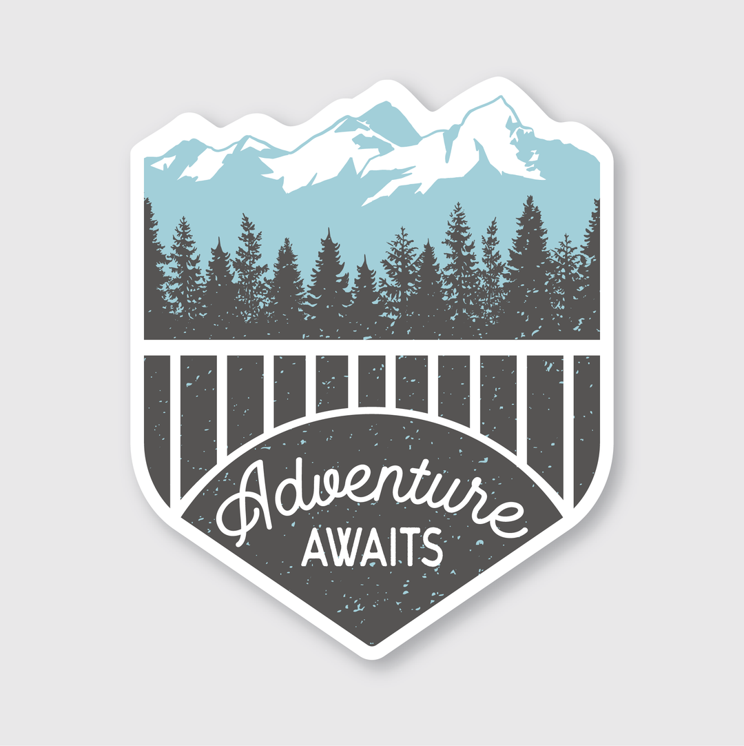 The Adventure Awaits Sticker features a die-cut vinyl design depicting a mountain range with pine trees in the foreground. The lower part of the sticker displays "Adventure Awaits" in decorative script. The mountains are depicted in light blue, while the trees and text are highlighted in black and white, celebrating independent artists.