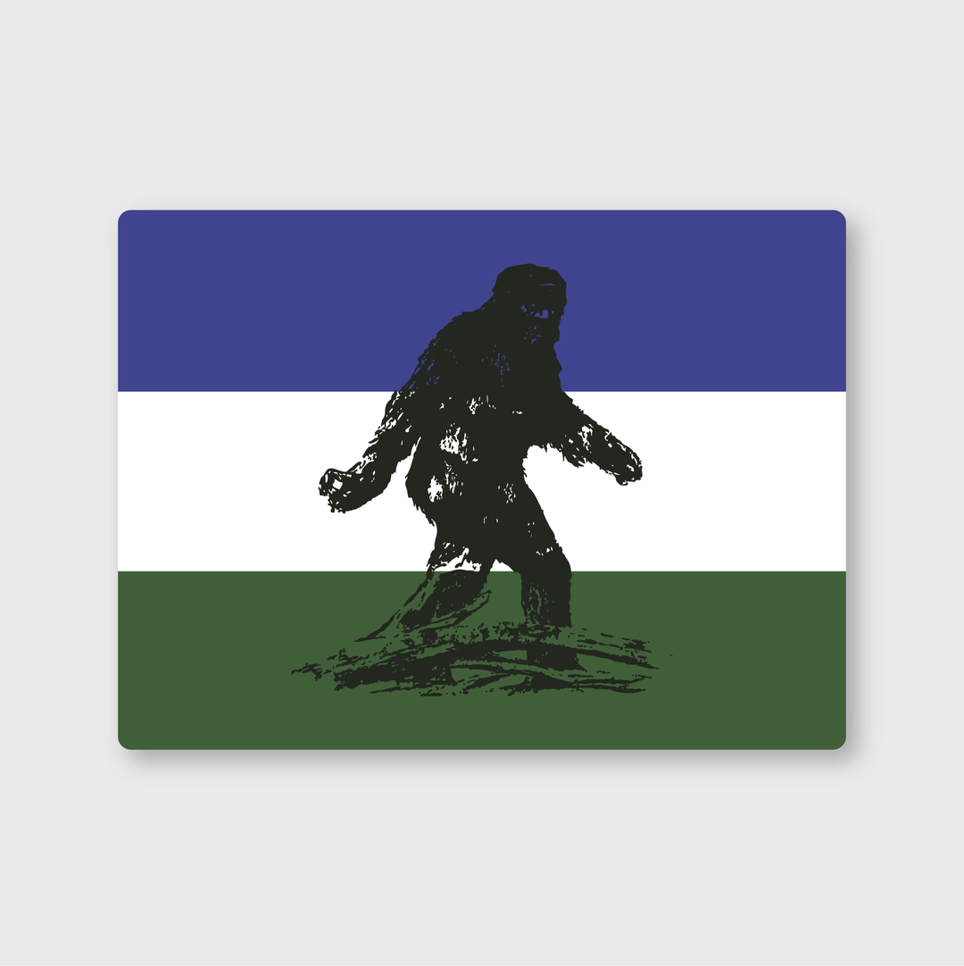 This sticker showcases a die-cut vinyl flag with the silhouette of Bigfoot set against three horizontal stripes: blue at the top, white in the middle, and green at the bottom. The design is whimsical and expertly crafted by talented artists from Seattle.