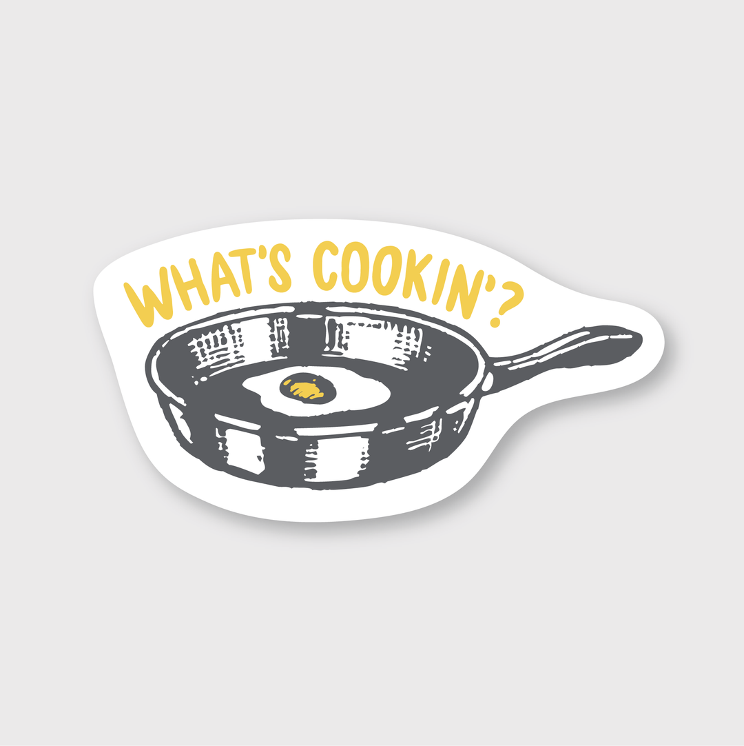 This "What's Cookin Sticker" is a die-cut vinyl piece featuring a retro-styled frying pan with a fried egg, and the phrase "WHAT'S COOKIN'?" above. It utilizes muted colors on a white background, offering both style and durability as it's weather-resistant, making it ideal for various placements.