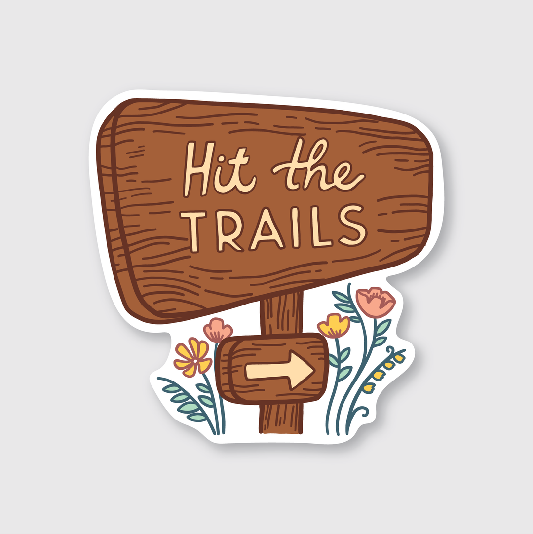 Explore the "Hit The Trails Sticker," a die-cut vinyl creation by Seattle artists. This sticker features a wooden sign with the phrase "Hit The Trails" accompanied by an arrow beneath it. The design is adorned with colorful flowers that add a touch of whimsy, making it visually striking. Made for durability in outdoor settings, its plain white background complements and enhances its vibrant design.