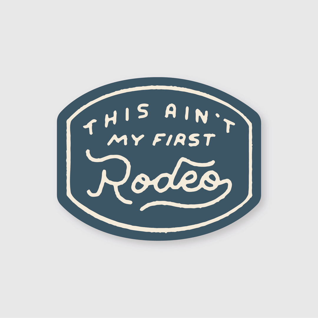 A die cut vinyl sticker titled "This Ain't My First Rodeo" features a blue, oval-shaped design with white text in a hand-drawn style font. The word "Rodeo" is beautifully highlighted with artistic swooshes. This unique, high-quality sticker is both water and weather resistant.